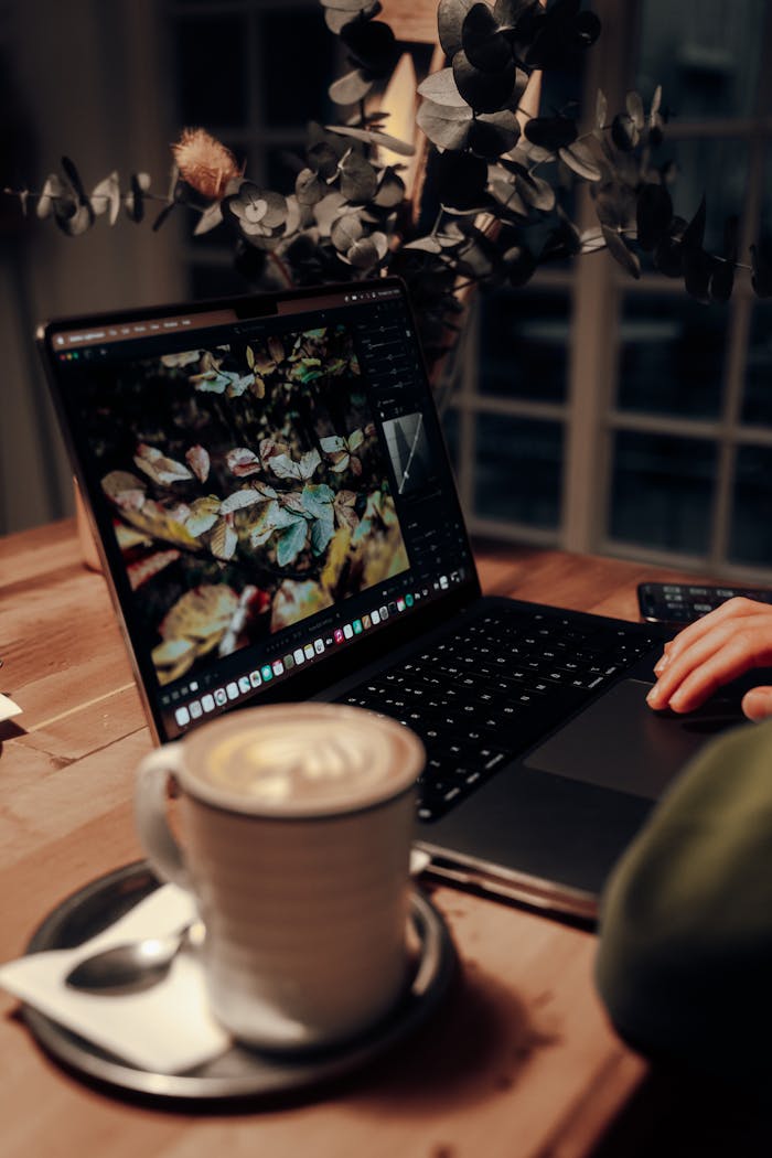 Services A cozy indoor workspace featuring a laptop and a steaming cup of cappuccino on a wooden desk.