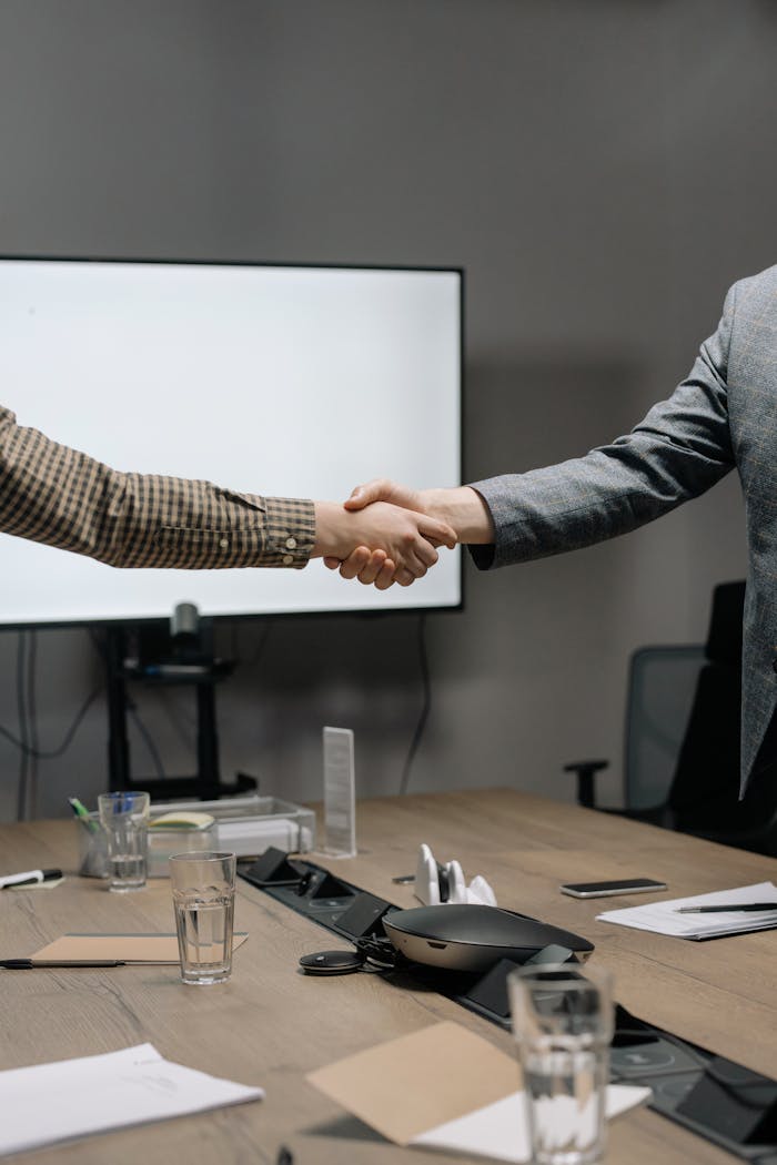 Services Two business professionals shaking hands in a modern meeting room, symbolizing successful collaboration.