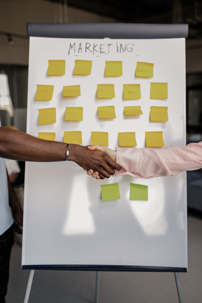 Services Colleagues shaking hands in front of a marketing board during a business meeting.